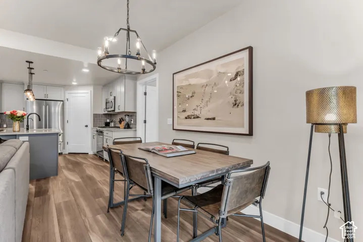 Dining area featuring wood-finish flooring, a circular wrought-iron chandelier, and recessed lighting, with kitchen showcasing stainless steel appliances and grey cabinetry