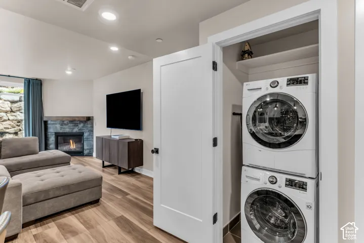 Stacked laundry unit housed within a closet, featuring wood-finish flooring, recessed lighting, and a stone-surround fireplace with a timber mantel