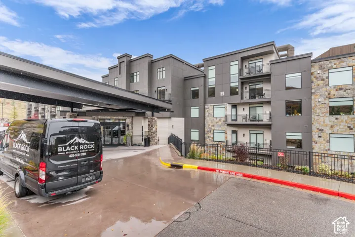 Multi-story exterior featuring stone veneer accents, flat-roof design, metal balcony railings, and a prominent covered porte-coch