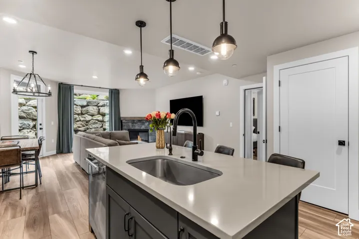 Kitchen island with composite stone countertop, stainless steel undermount sink, matte black gooseneck faucet, wood-finish flooring, and industrial-style pendant lighting