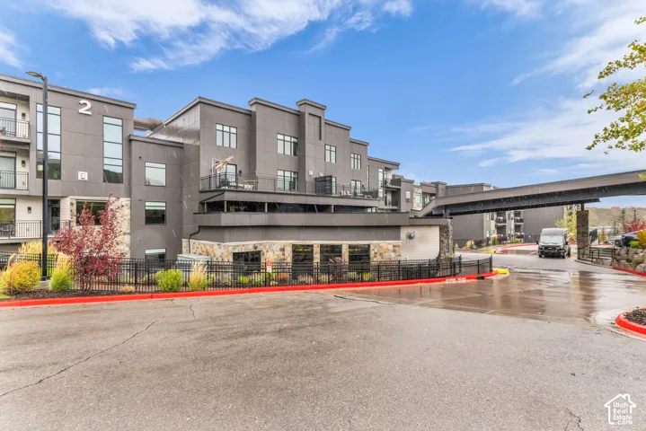 Modern multi-story exterior featuring dark paneling, natural stone accents, private balconies, and an attached covered walkway