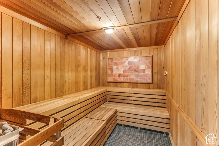 Sauna featuring natural wood wall and ceiling paneling, tiered wood bench seating, a decorative stone-inlaid panel, and dark mosaic tile flooring