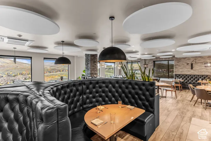 Open-concept space featuring tufted leather built-in booths, wood-finish flooring, ceiling-mounted acoustic panels, stone-accented walls, and oversized dome pendant lighting