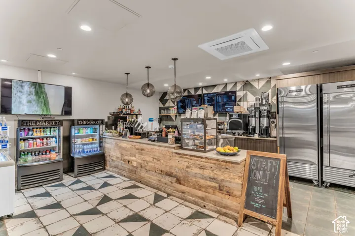 Commercial retail space featuring a rustic wood-plank service counter, patterned tile flooring, stainless steel refrigeration units, pendant globe lighting, and a geometric-tiled backsplash