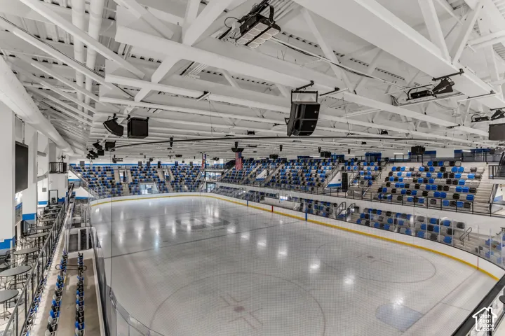 Indoor ice rink featuring vaulted ceiling trusses, tiered spectator seating, protective glass dasher boards, and overhead audio equipment