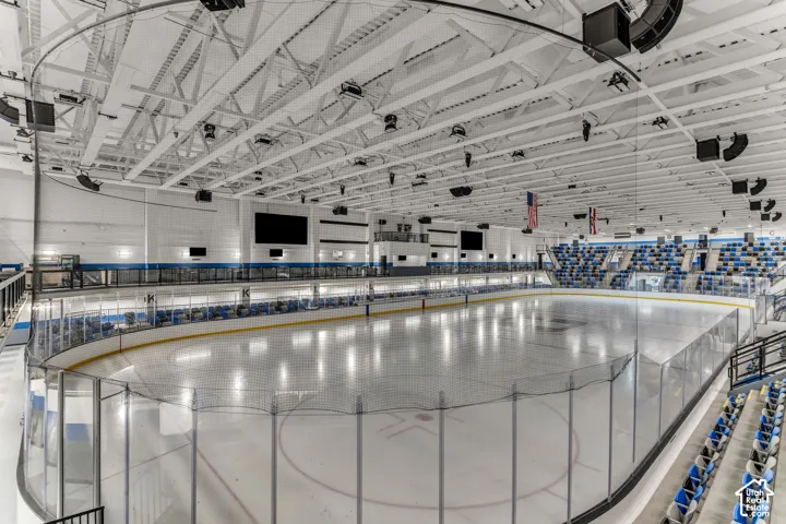 Indoor ice rink featuring an expansive surface, protective dasher boards with glass shielding, overhead industrial lighting, and tiered stadium seating