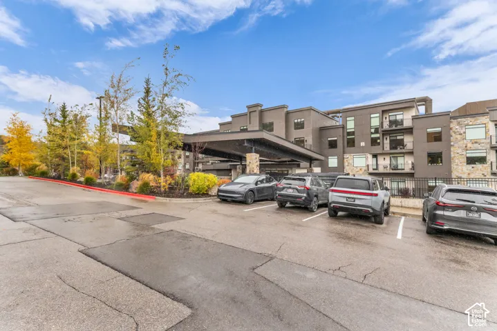 Multi-story complex exterior featuring a porte-cochere, stone veneer accents, stucco facade, balconies, and asphalt surface parking