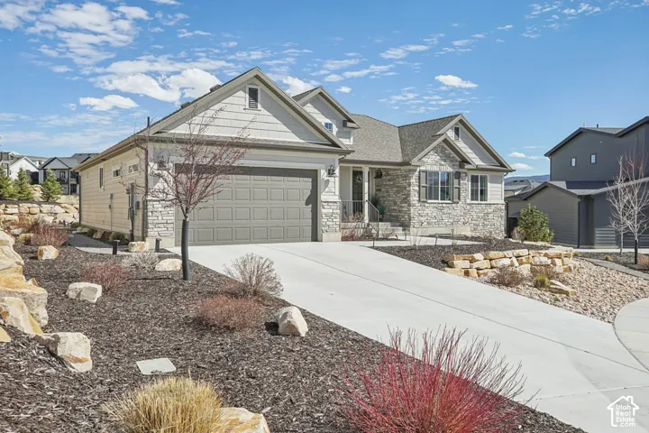 Single-level exterior featuring stone veneer accents, horizontal lap siding, a two-car garage, and tiered stone retaining walls with decorative landscaping