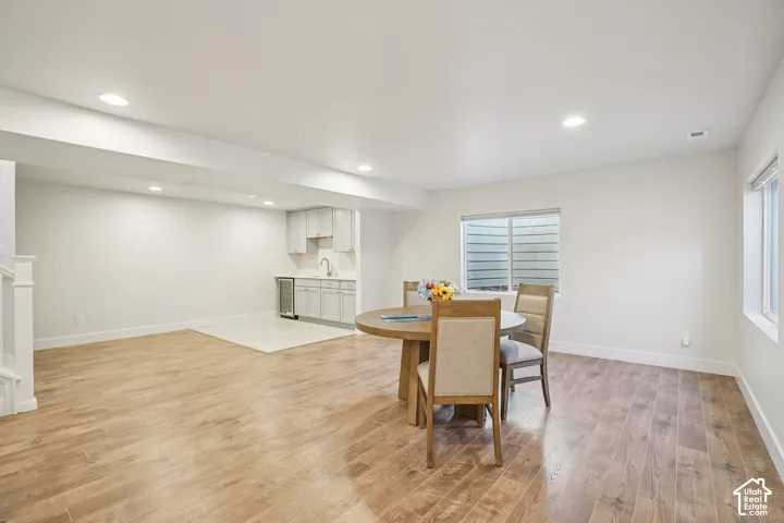 Open-concept area featuring wood-finish flooring, recessed lighting, and a kitchenette with neutral cabinetry, a stainless steel beverage refrigerator, and a sink