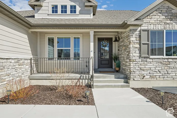 Front exterior featuring a stone veneer facade, horizontal siding, covered concrete porch with metal railings, and a multi-pane glass entry door