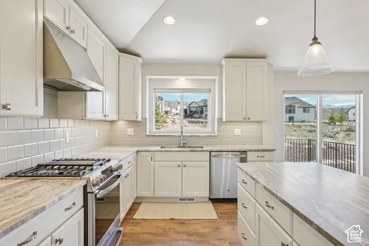 Kitchen featuring white shaker-style cabinetry, stone-finish countertops, stainless steel appliances, a tile backsplash, and wood-finish flooring