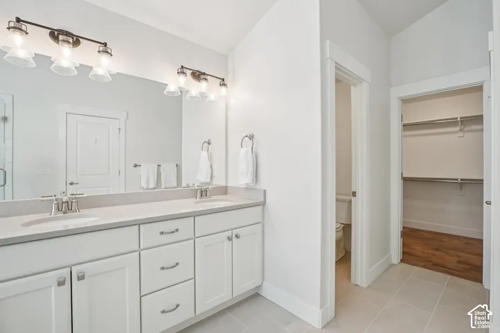 Dual-sink vanity with white shaker-style cabinetry, quartz countertops, full-width vanity mirror, dual wall-mounted light fixtures, and ceramic tile flooring