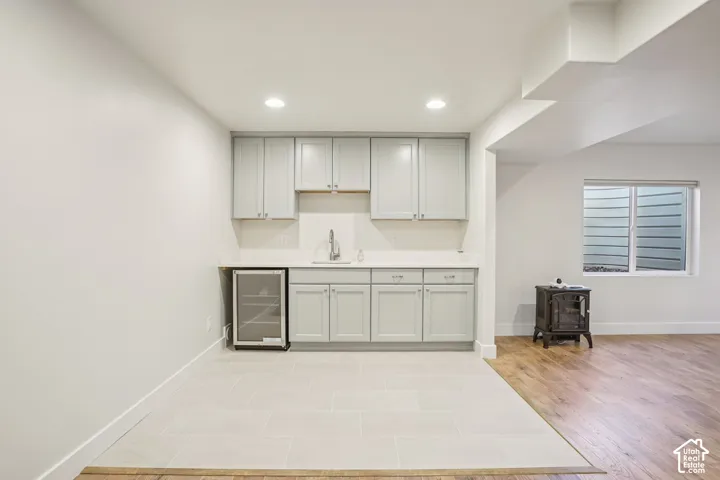 Kitchenette featuring shaker-style cabinetry, a stone-finish countertop, under-mount sink, built-in beverage refrigerator, and neutral tile flooring