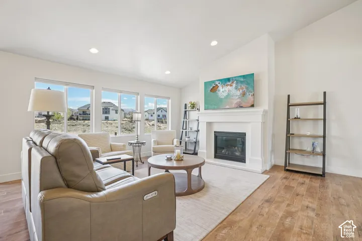 Living area featuring wood-finish flooring, vaulted ceilings, recessed lighting, and a fireplace with a white mantel surround