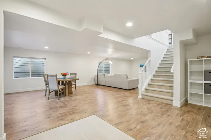 Open-concept floor plan featuring wood-finish flooring, recessed lighting, carpeted staircase with white railings, and two window wells