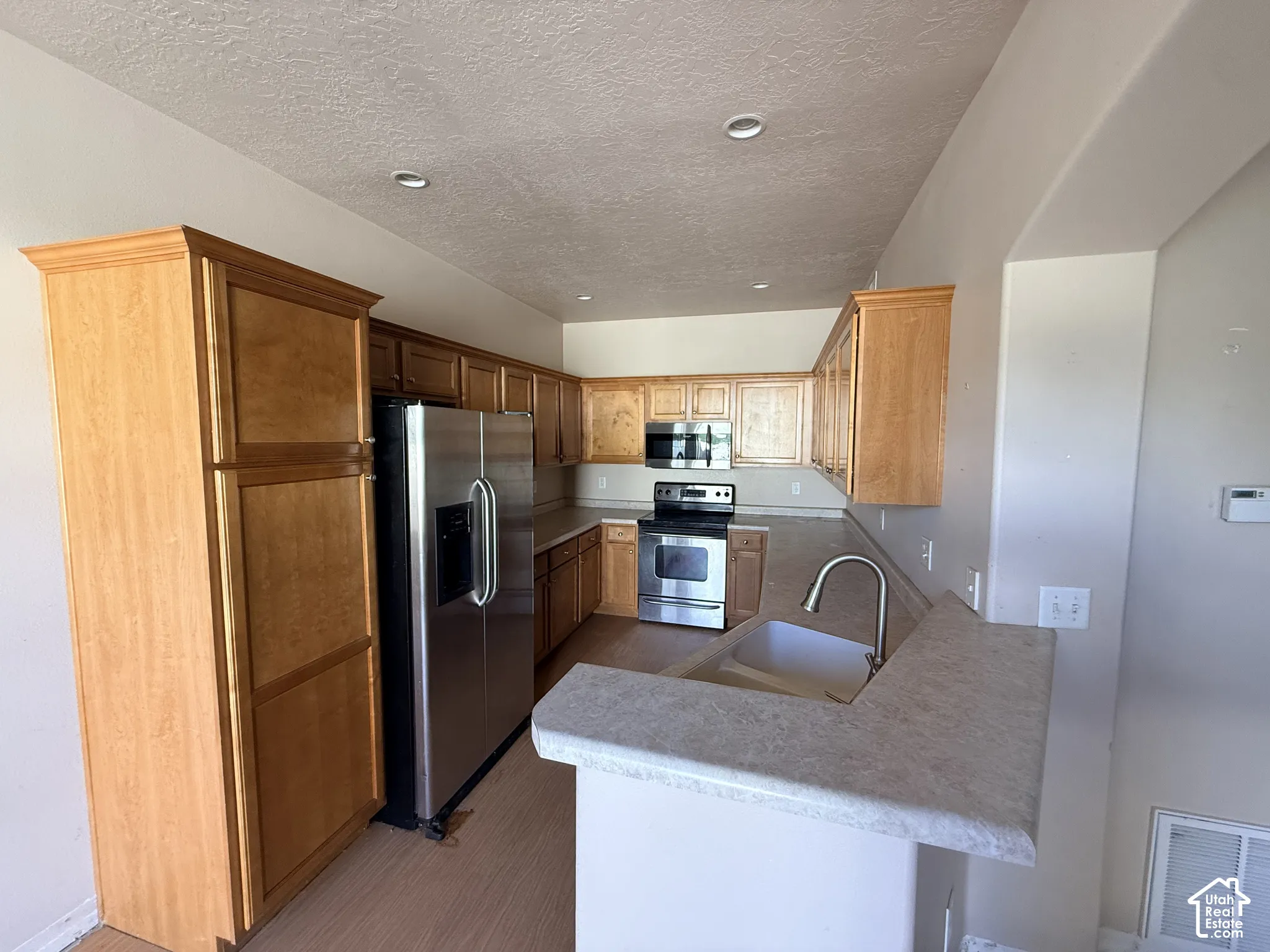 Kitchen featuring wood cabinetry, stainless steel appliances, neutral countertops, recessed lighting, and a dual-basin sink with a gooseneck faucet