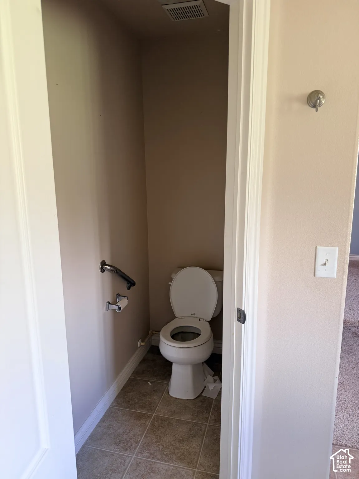 Enclosed water closet featuring tile flooring, a wall-mounted grab bar, and a standard-height toilet