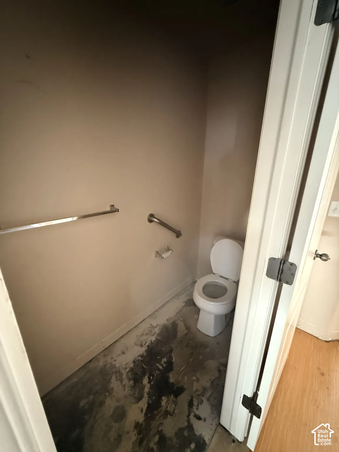 Enclosed space featuring a white toilet, wall-mounted brushed metal grab bars, and a coordinating metal toilet paper holder