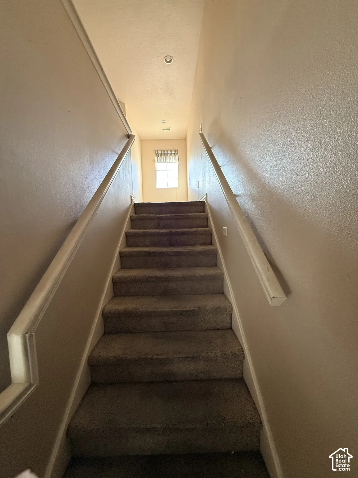 Staircase featuring wall-mounted wooden handrails and carpeted treads