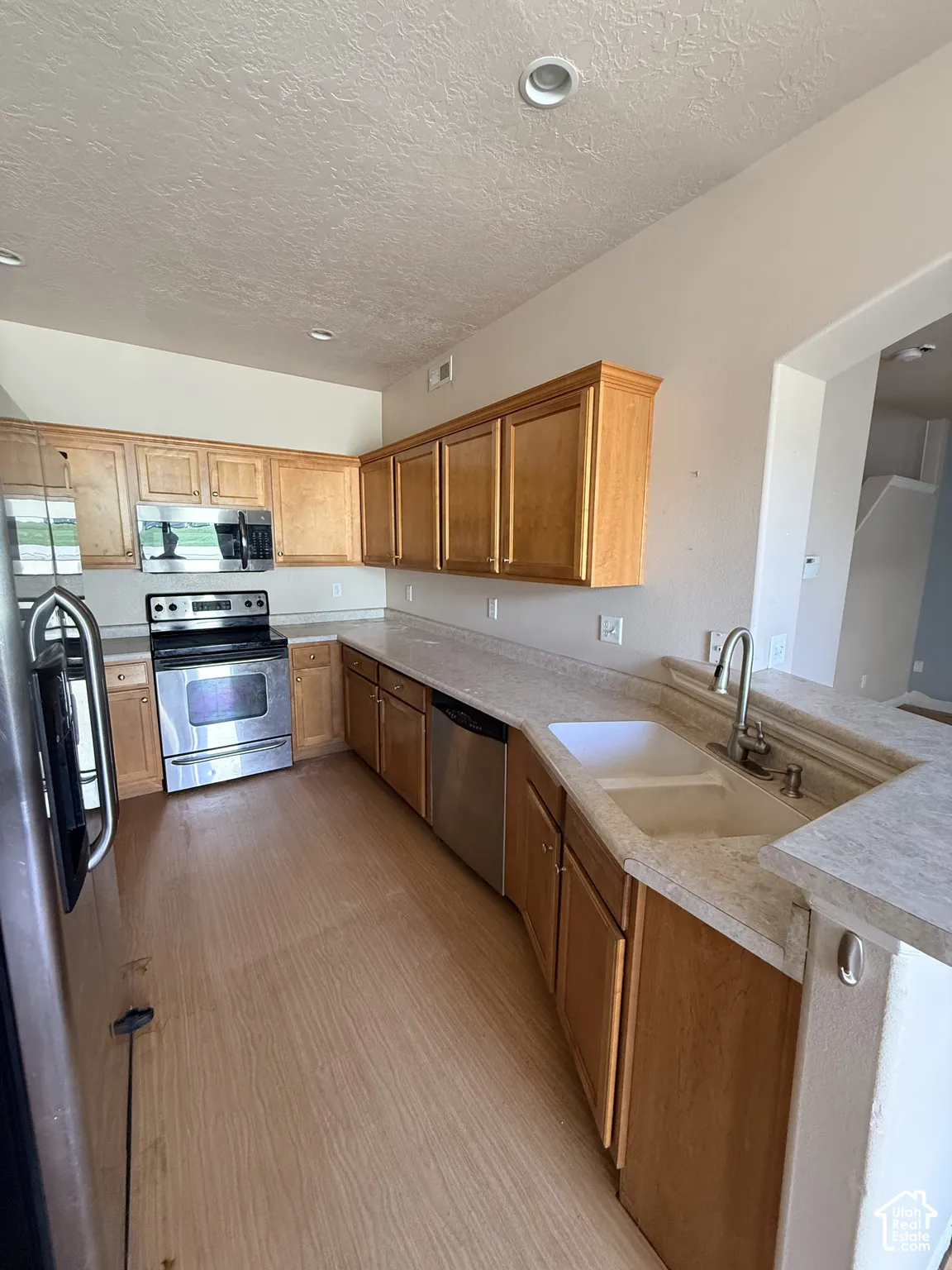 Kitchen featuring wood cabinetry, stainless steel appliances, dual-basin sink with high-arc faucet, and neutral laminate countertops