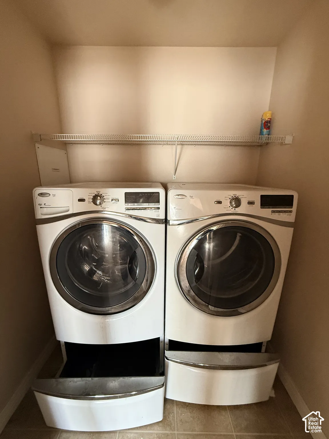 Laundry area featuring front-loading machines with integrated storage pedestals and an overhead wire shelving unit