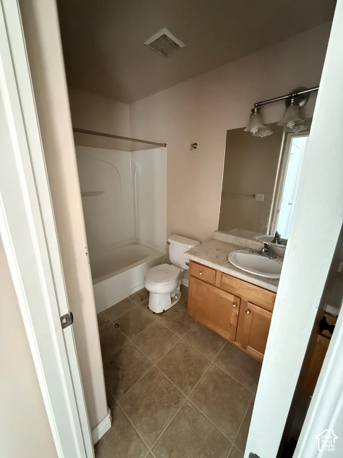 Bathroom featuring tile flooring, a composite-top vanity with built-in cabinetry, a chrome-finish multi-light wall fixture, and a white acrylic shower-tub surround