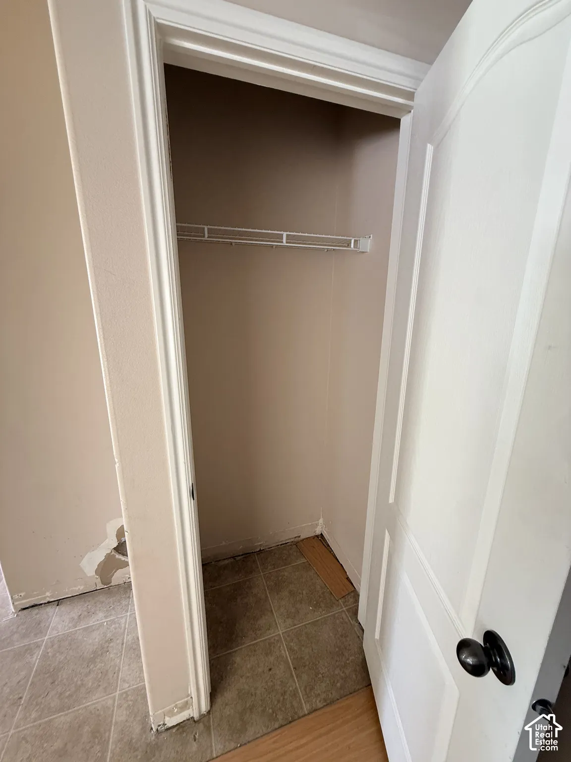 Storage closet featuring a white-paneled door, black hardware, and an integrated shelf