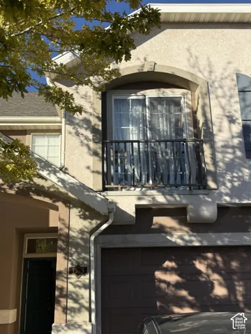 Stucco exterior featuring an arched upper-level balcony with a black metal railing and a multi-panel sliding glass door