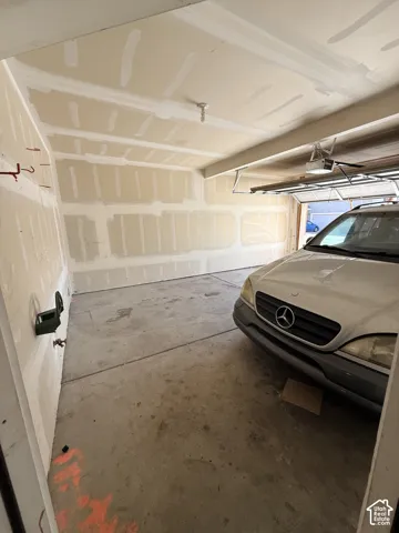 Garage featuring unfinished drywall, concrete flooring, overhead garage door opener, and water spigot
