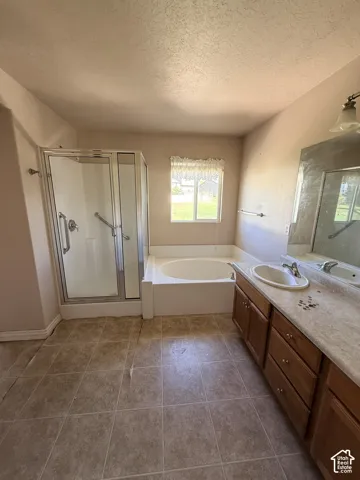 Bathroom featuring a glass-enclosed shower, soaking tub, wooden cabinetry, vanity with an integrated sink, and tile flooring