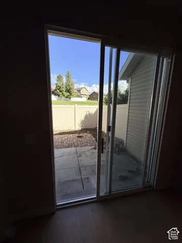 Sliding glass patio door opening to a concrete and paver patio, enclosed by a white vinyl privacy fence