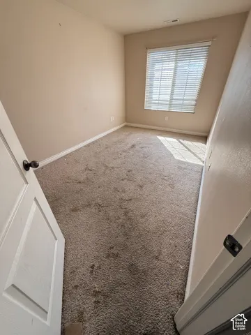 Neutral-toned interior space featuring carpeting, smooth wall finishes, and a window with horizontal blinds