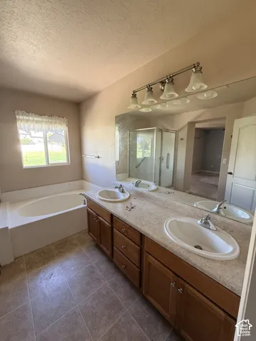 Dual-sink vanity with light-tone solid surface countertop, wood cabinetry, large soaking tub, tile flooring, and integrated shower stall