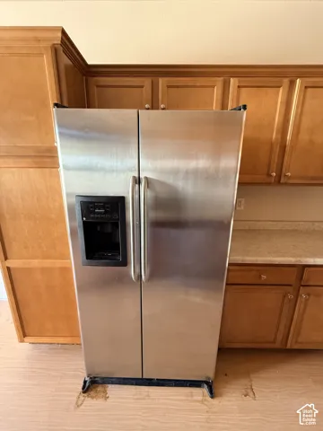 Stainless steel side-by-side refrigerator with exterior water and ice dispenser, light-tone wood-finish cabinetry, and laminate countertop