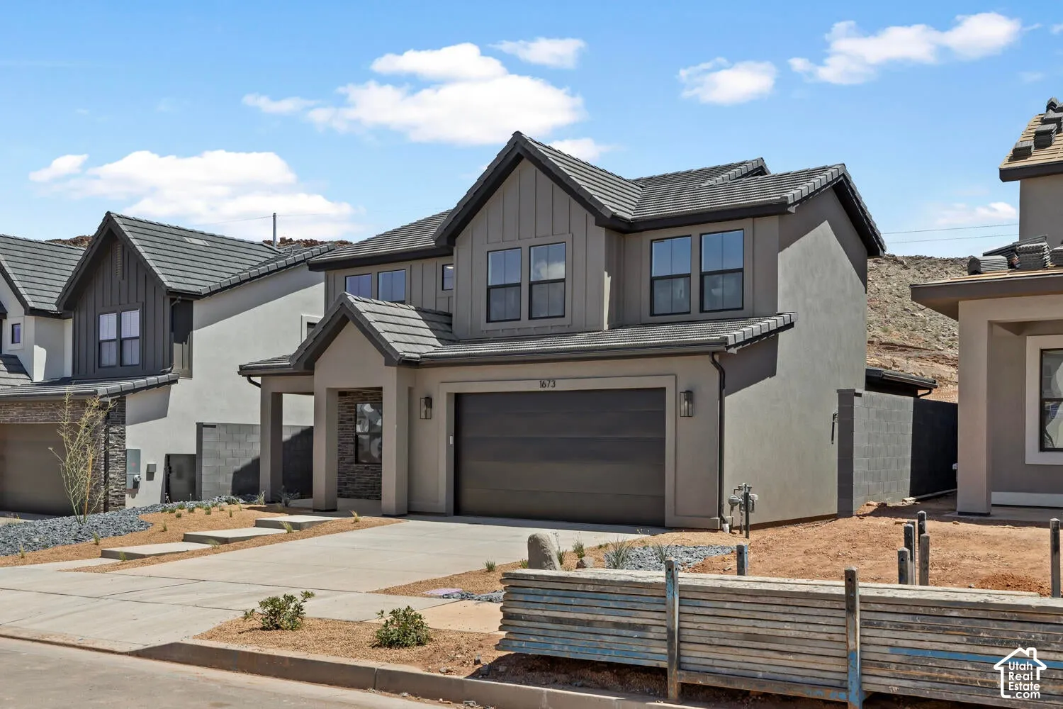 Two-story exterior featuring a grey stucco facade, vertical siding accents, dark-toned concrete roof tiles, and an attached two-car garage