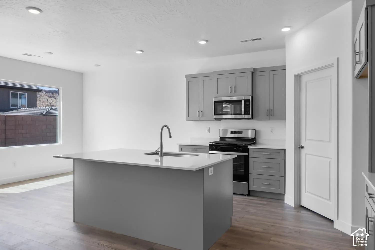 Kitchen featuring a center island with a quartz countertop, gray shaker-style cabinetry, stainless steel appliances, and wood-finish flooring