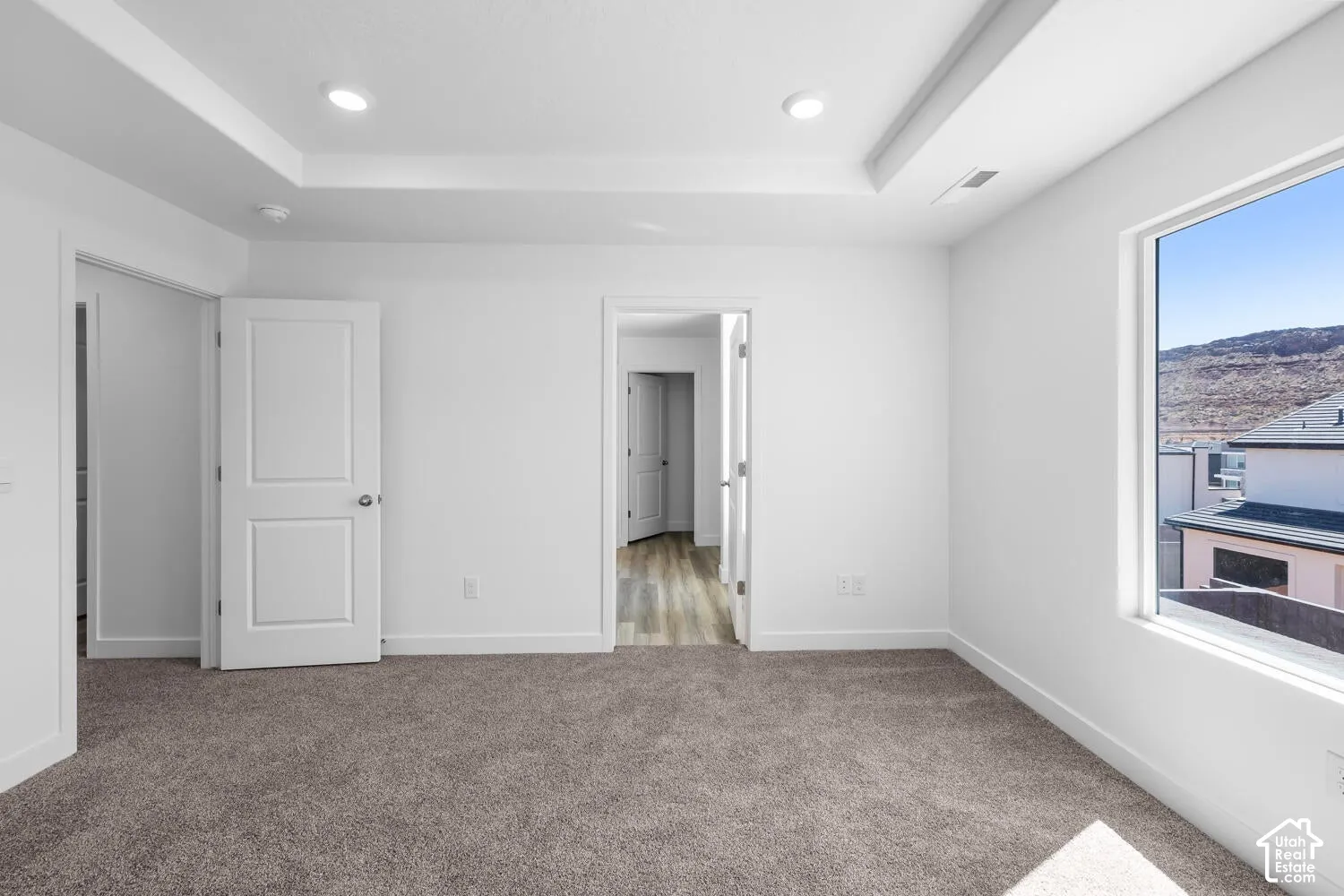 Tray ceiling featuring recessed lighting, plush wall-to-wall carpeting, and a large picture window showcasing mountain scenery