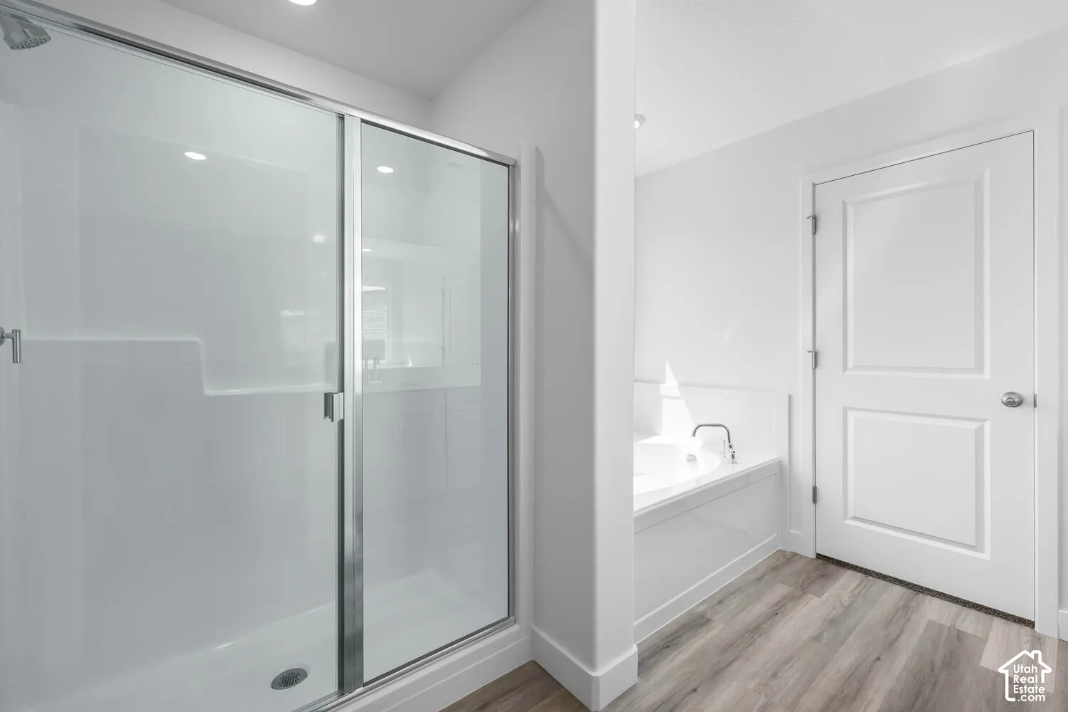 Walk-in shower with sliding glass doors, built-in soaking tub, and wood-finish flooring