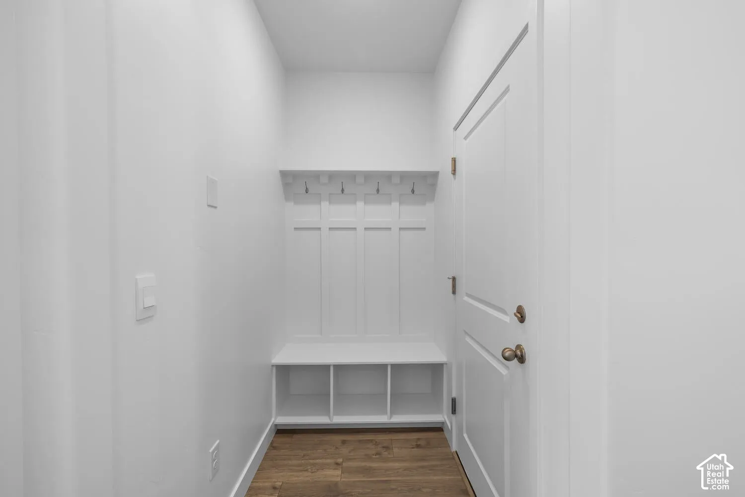 Built-in bench with four-section cubby storage, vertical board-and-batten wall detailing, integrated overhead shelf, four wall-mounted hooks, and wood-finish flooring