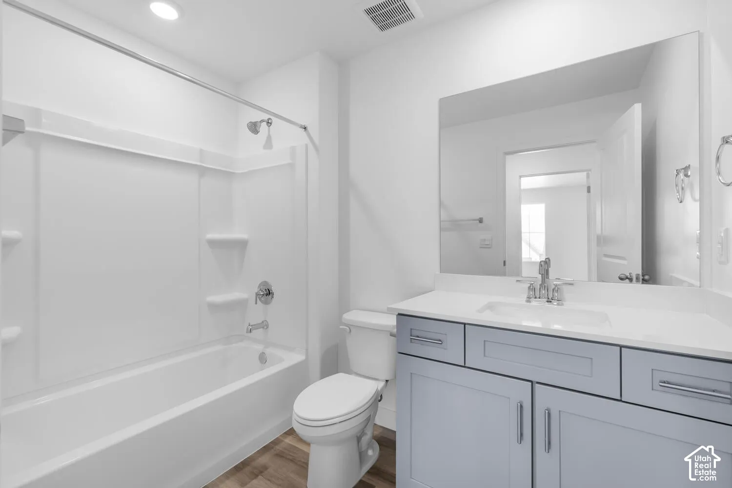 Bathroom featuring a gray shaker-style vanity, white countertop with an integrated sink, polished chrome faucet, full-width vanity mirror, and a white bathtub-shower surround