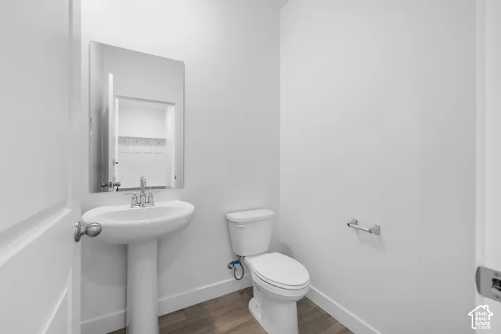 Bathroom featuring a pedestal sink, wall-mounted mirror, white ceramic toilet, and wood-finish flooring