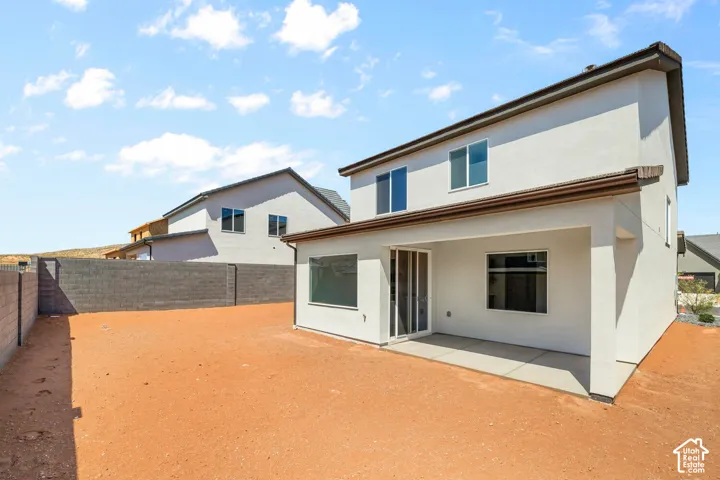 Two-story exterior featuring light-colored stucco siding, a covered concrete patio, sliding glass doors, and a masonry perimeter wall