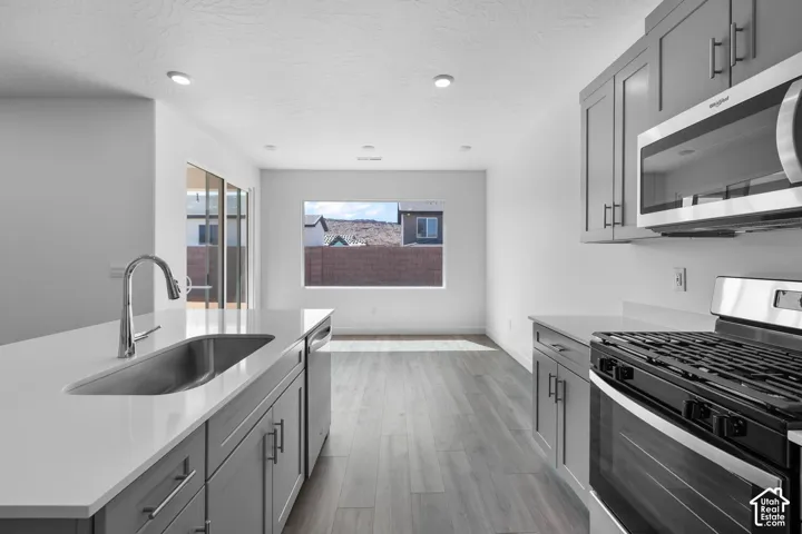 Kitchen featuring gray shaker-style cabinetry, quartz countertops, stainless steel undermount sink with high-arc faucet, stainless steel gas range, and wood-finish flooring