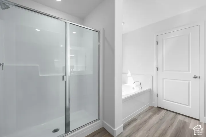 Walk-in shower with sliding glass doors, built-in soaking tub, and wood-finish flooring