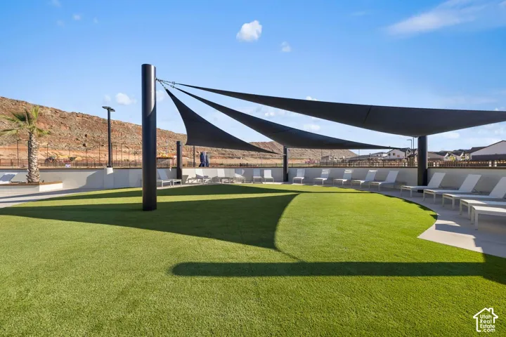 Outdoor recreation area featuring artificial turf, a large structural shade sail, a concrete perimeter wall, and integrated pole lighting