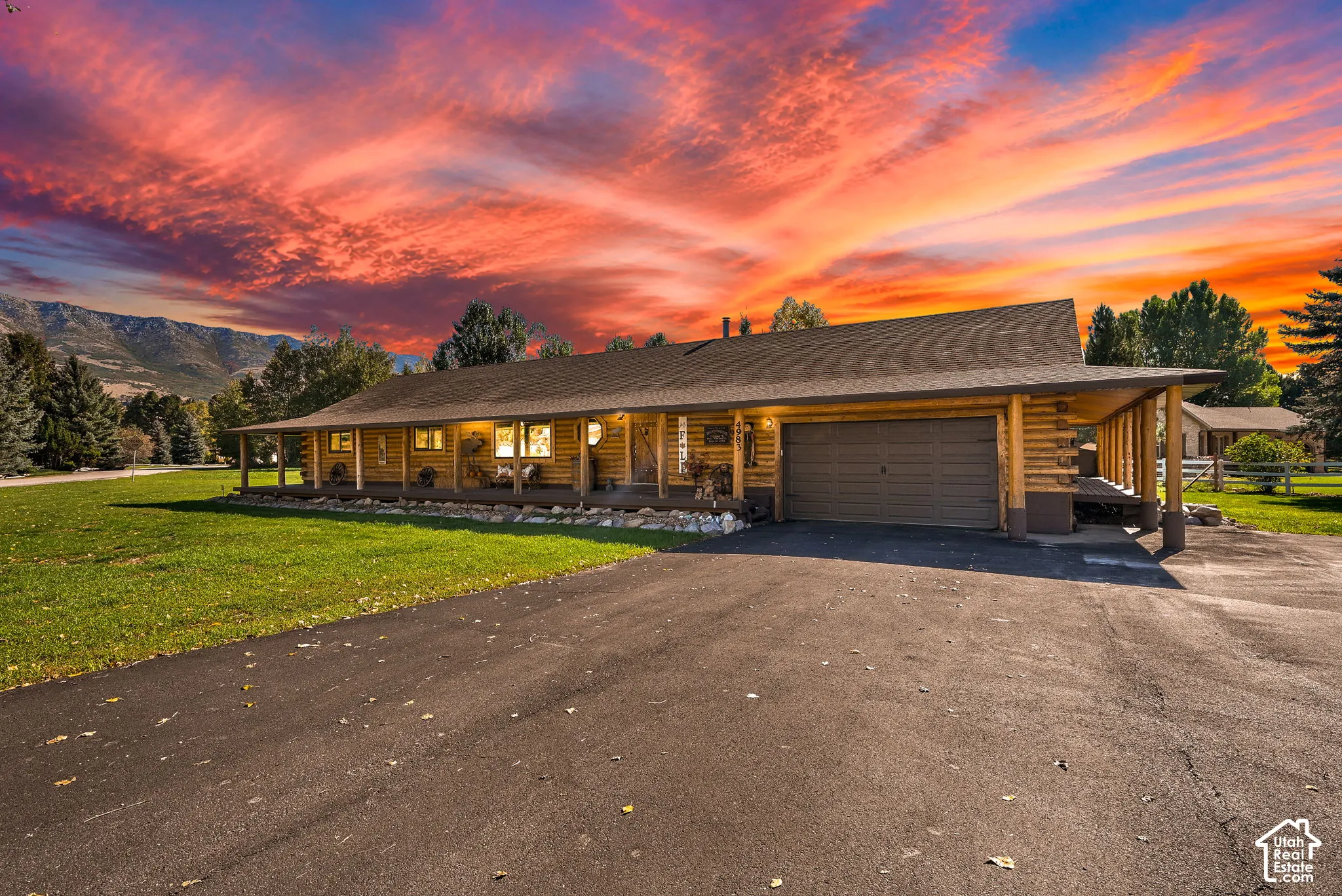 Log cabin exterior with a covered porch, attached garage, paved driveway, and mountain views