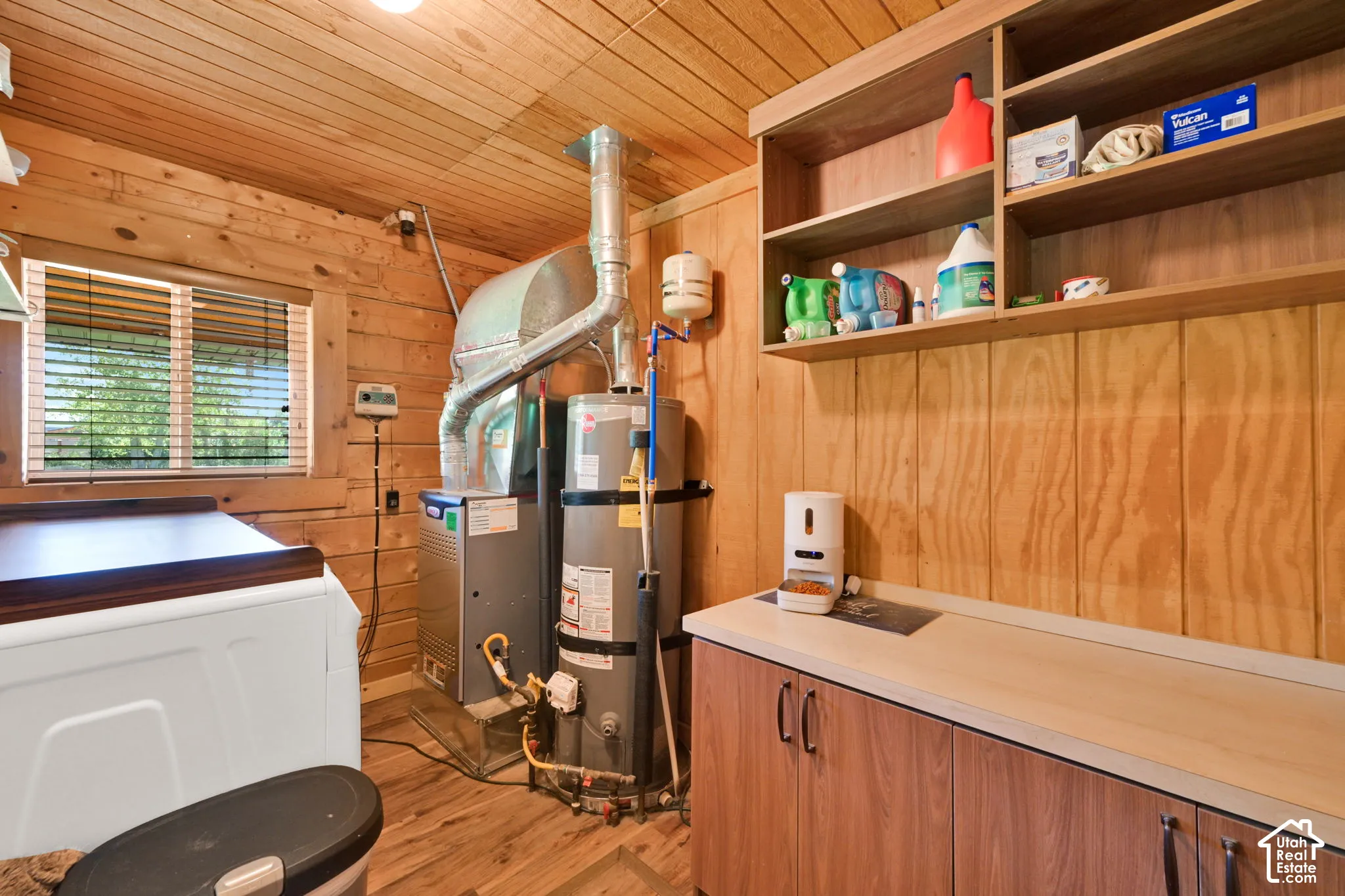 Utility room featuring wood-paneled walls and ceiling, built-in lower cabinetry with laminate countertop, and open wood shelving