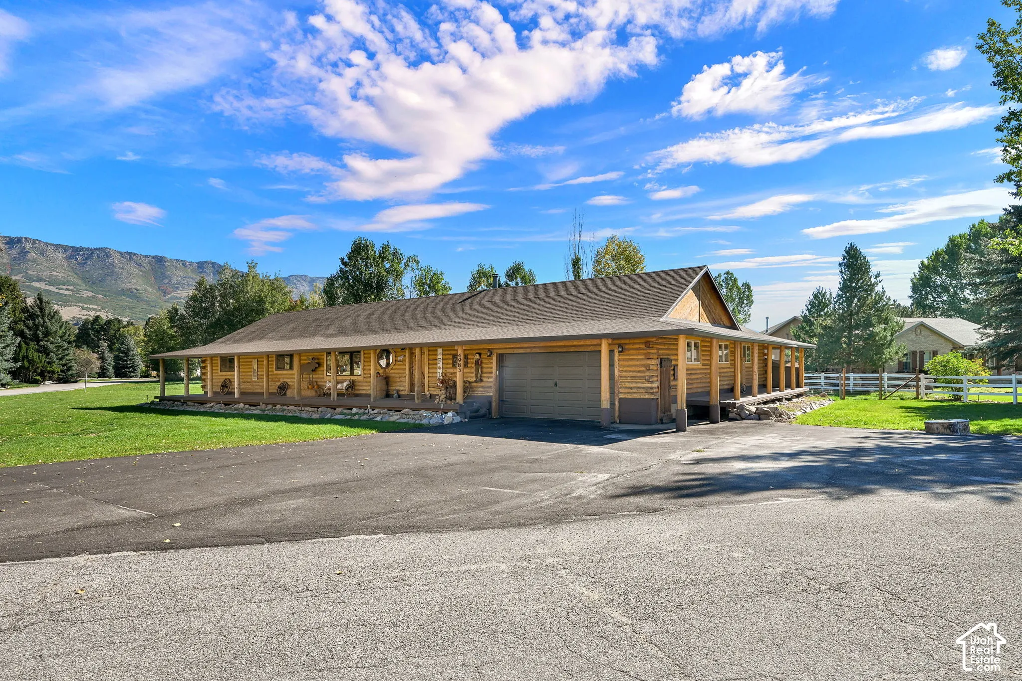 Log cabin exterior with a covered porch, attached garage, paved driveway, and mountain views
