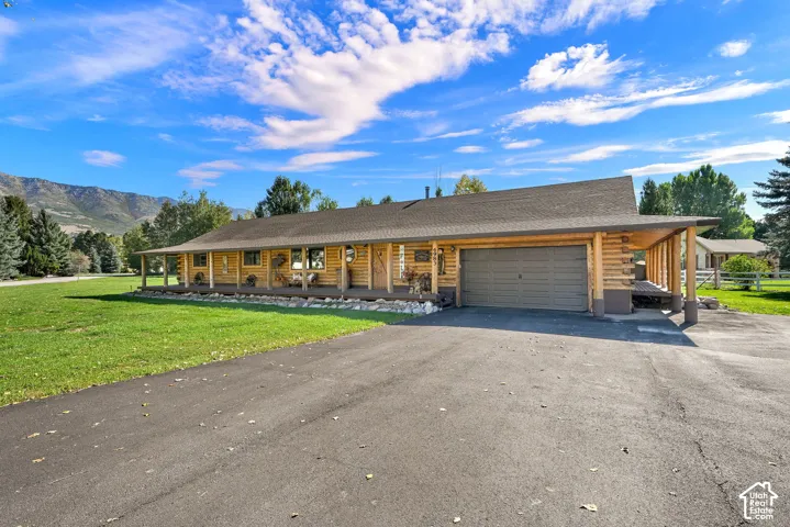 Log cabin exterior with a covered porch, attached garage, paved driveway, and mountain views