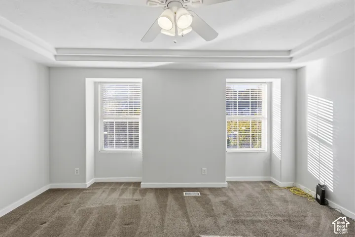 Tray ceiling with a central three-light ceiling fan, neutral wall tones, and recessed window alcoves featuring integrated horizontal blinds